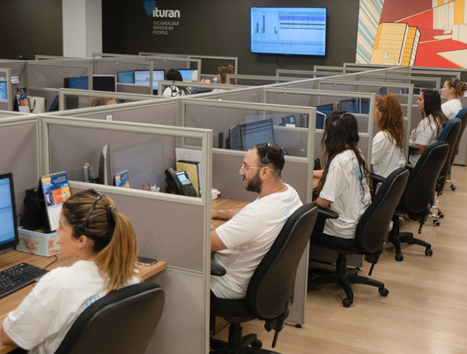 Ituran employees work at computer workstations in the mobility technology company's modern office, with the Ituran logo and digital displays visible in the background.